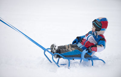 Boy sitting on sled at covered field