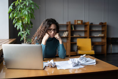 Frowning businesswoman at desk look at crumpled papers. office worker or writer tired of paperwork