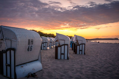 Hooded chairs on beach against sky during sunset