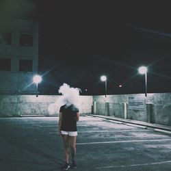 Rear view of woman standing on illuminated street at night