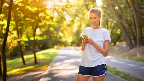 Full length of woman holding smart phone while standing on tree