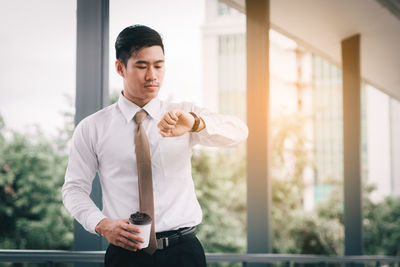 Businessman checking time while standing against window in office