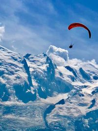 Person paragliding over snowcapped mountain against sky