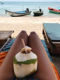 Midsection of woman with coconut sitting on lounge chair at beach