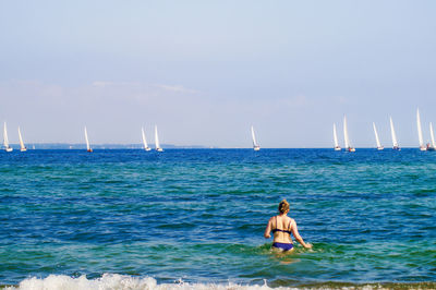Rear view of men on sailboat in sea against sky