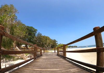 Footbridge amidst trees against clear blue sky