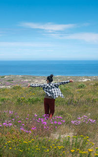 Rear view of woman standing by plants against sea and sky