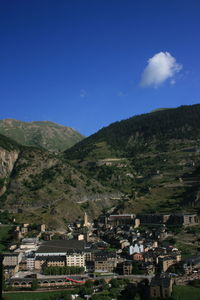Scenic view of townscape by mountains against blue sky