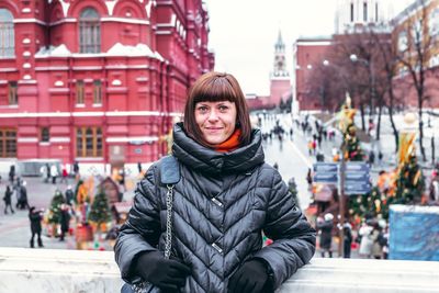Portrait of smiling young woman standing in city during winter