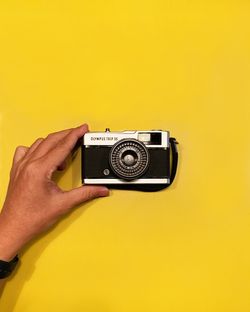 Close-up of hand holding camera against yellow background