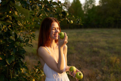 Young woman holding apple while standing outdoors