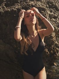 Young woman wearing swimsuit standing against rock