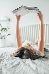 Cute girl reading book while lying on bed at home