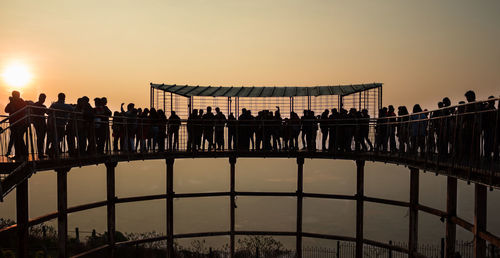 Silhouette people on bridge against sky during sunset