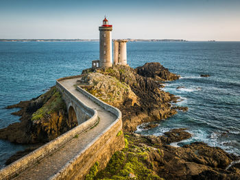 Lighthouse amidst sea and buildings against sky in brittany at the golden hour