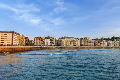 Buildings by sea against blue sky