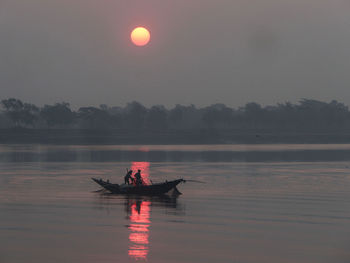 Man in boat on river against sky during sunrise.