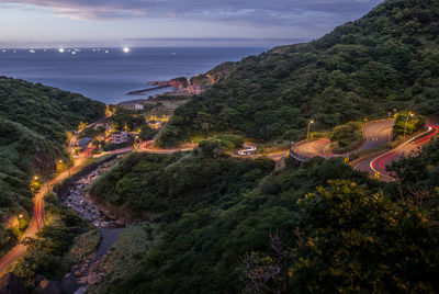 High angle view of illuminated city by sea against sky