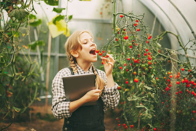 Young woman using phone while standing on plants