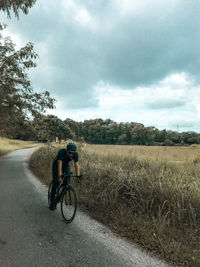 Rear view of man riding bicycle on field against sky