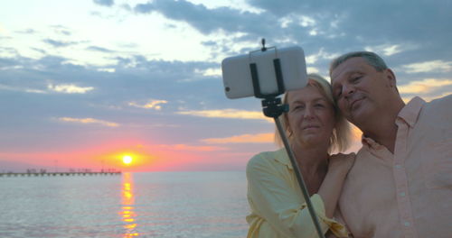 Portrait of man photographing sea against sky during sunset