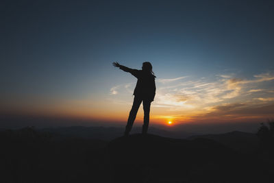 Silhouette man standing on rock against sky during sunset