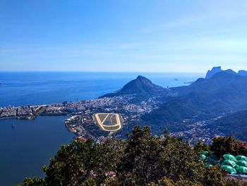 High angle view of city by sea against blue sky