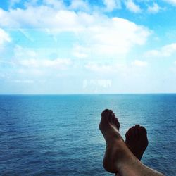 Low section of man relaxing on sea against sky