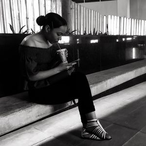 Young woman using smart phone while sitting on laptop