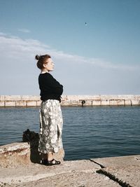 Side view of woman standing by sea against sky