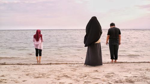 Rear view of people standing on shore at beach