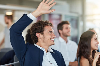 Smiling colleague with hand raised during meeting at office