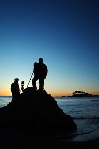 Silhouette man standing on shore against clear sky during sunset