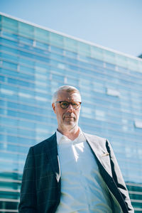 Low angle portrait of senior businessman standing against modern building