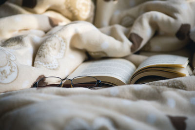 Close-up of open book and eyeglasses on bed