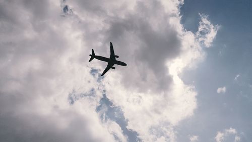 Low angle view of airplane flying against cloudy sky