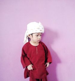 Cute boy wearing traditional clothing standing against pink wall