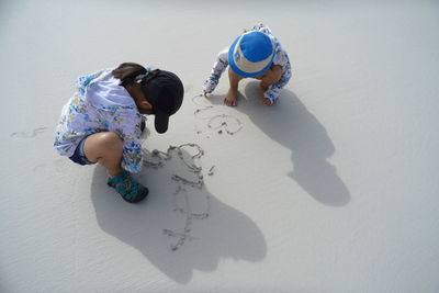 High angle view of siblings writing on sand at beach
