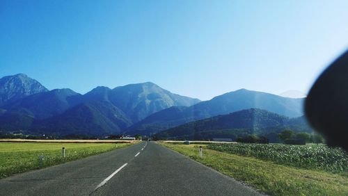 Road leading towards mountains against clear sky