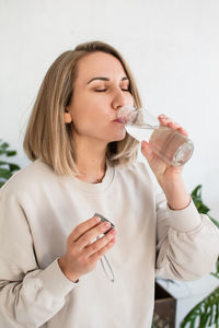 Young blonde woman is holding a glass bottle of water and drinking, healthy lifestyle,water balance