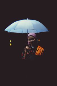 Young woman holding umbrella while standing against black background