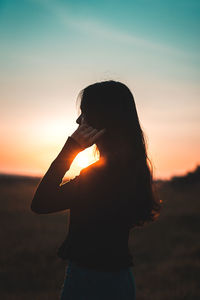 Side view of beautiful woman standing against sunset