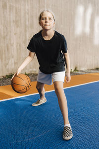 Portrait of girl dribbling basketball at sports court