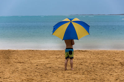 Rear view of boy standing on beach with umbrella