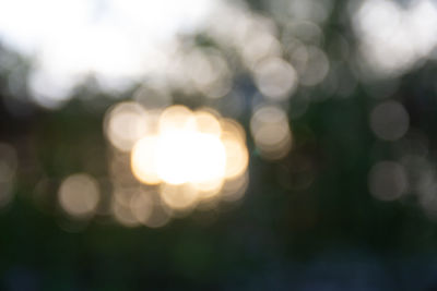 Defocused image of illuminated lights against sky at sunset