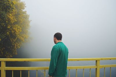 Rear view of man standing by railing against sky