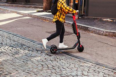 Low section of woman riding push scooter on footpath