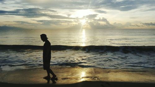 Silhouette man walking on shore against sea during sunset