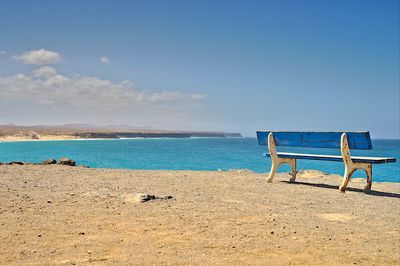 Empty chairs on beach against sky