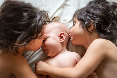 Two elder children kissing perplexed newborn baby